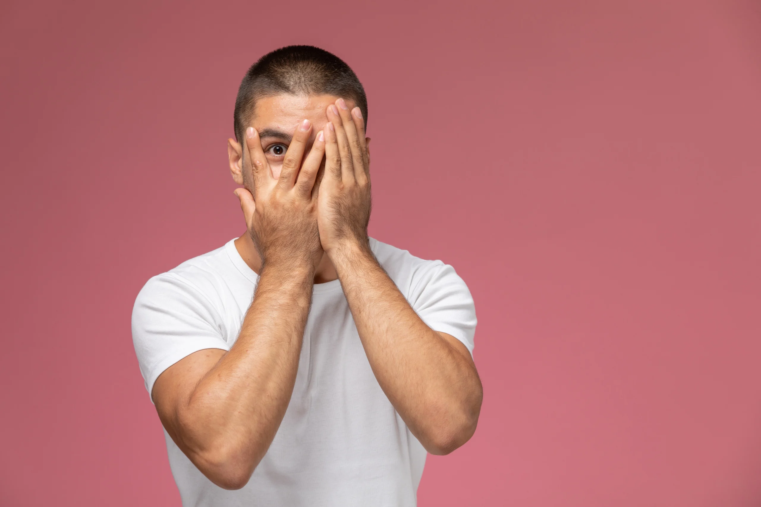 A young male wearing white shirt covering his face as he is afraid of the social consequences of facial surgery